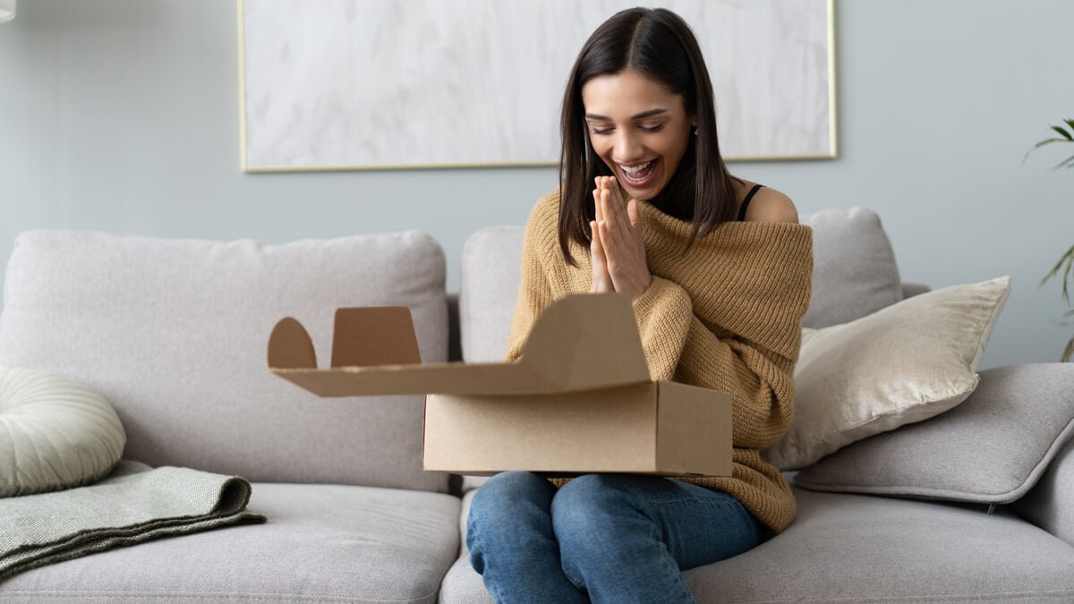 Jeune femme heureuse découvrant le contenu d’une Mystery Box dans son salon cosy